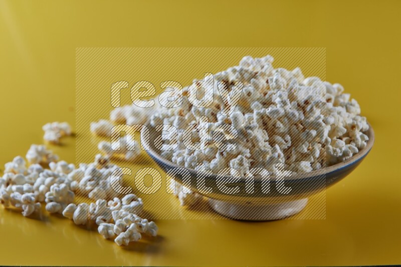 A multicolored ceramic plate full of popcorn with popcorn beside it on a yellow background in different angles