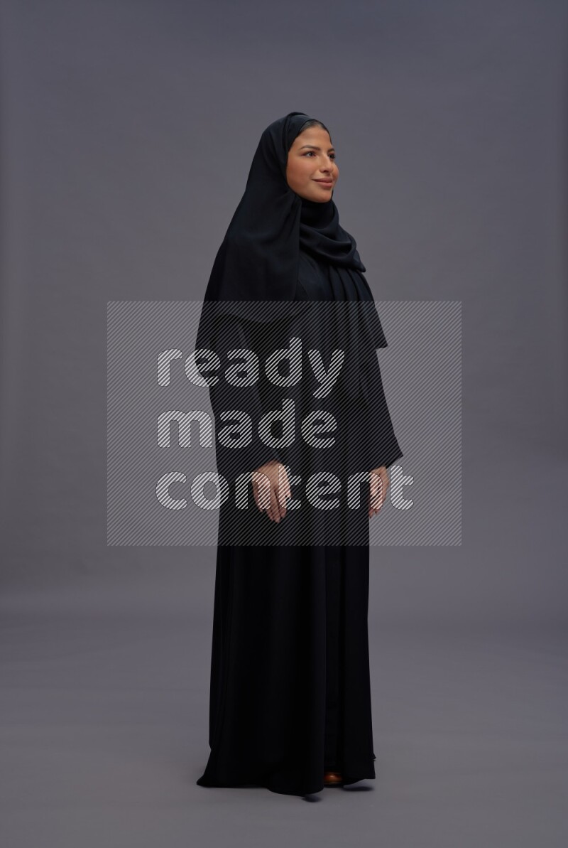 Saudi woman wearing Abaya standing interacting with the camera on gray background