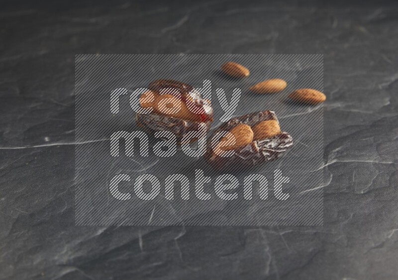 two almond stuffed madjoul dates on a black textured background
