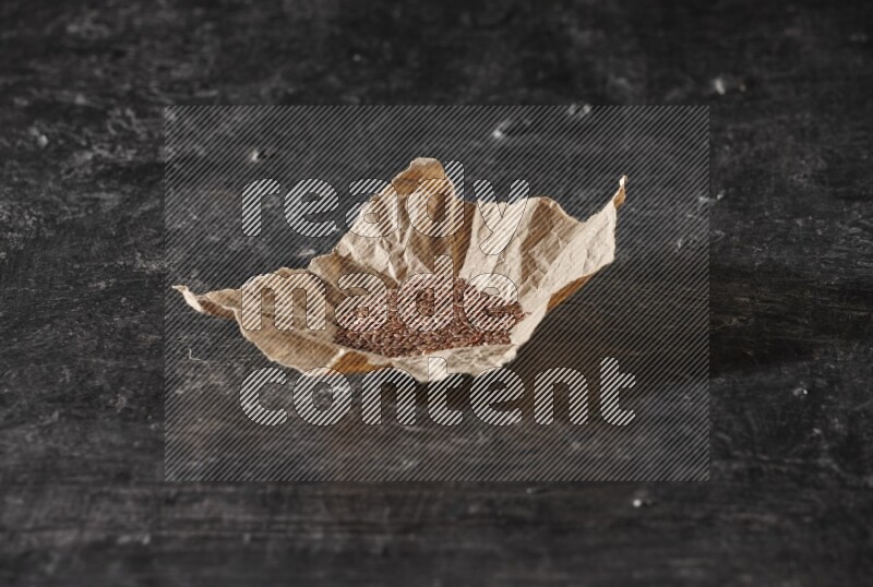 A crumpled piece of paper full of flaxseeds on a textured black flooring