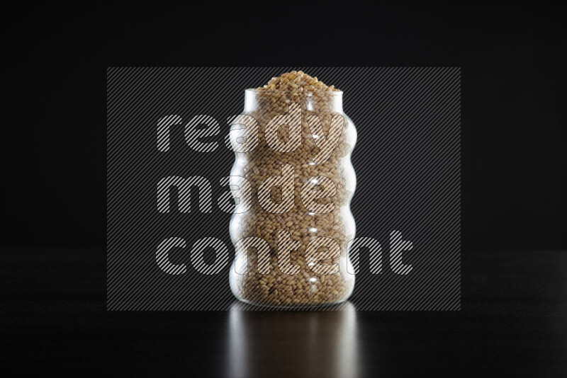 Hulled wheat in a glass jar on black background