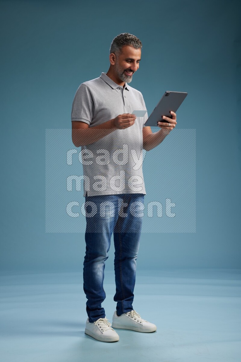 Man Standing holding ATM while working on tablet on blue background