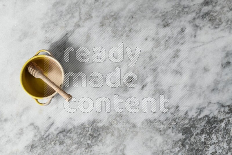 Multicolored pottery bowl with wooden honey dipper in it on grey marble background