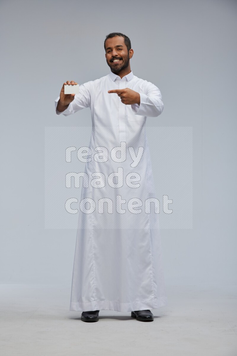Saudi man wearing Thob standing holding ATM card on Gray background