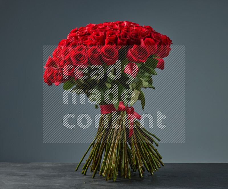 A luxurious bouquet of red roses tightly bound with a red ribbon on black marble background