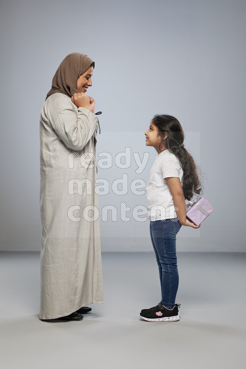 A girl standing hiding a gift behind her back for her mother on gray background