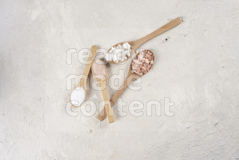 4 wooden spoons filled with fine and coarse salt on white background