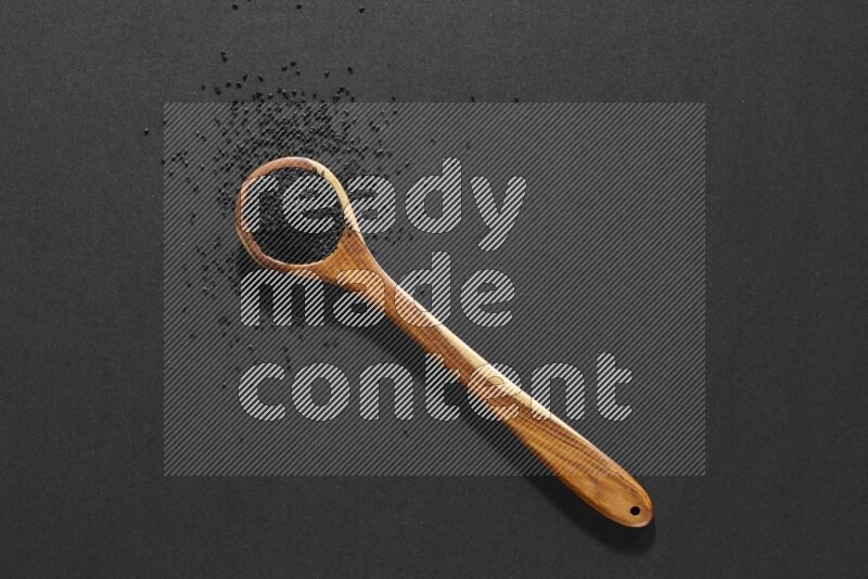 A wooden ladle full of black seeds and the seeds spread beside it on a black flooring