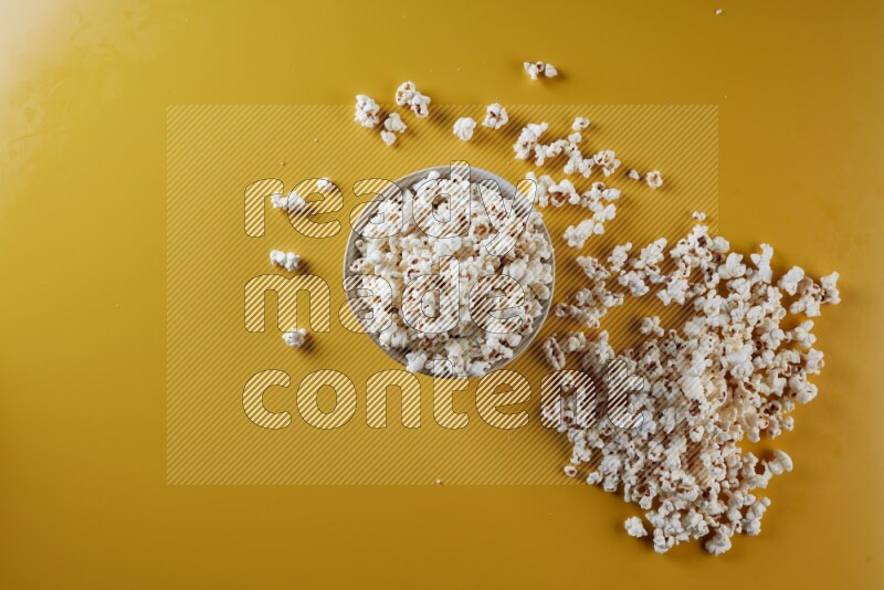 A white pottery bowl full of popcorn with popcorn beside it on a yellow background in different angles