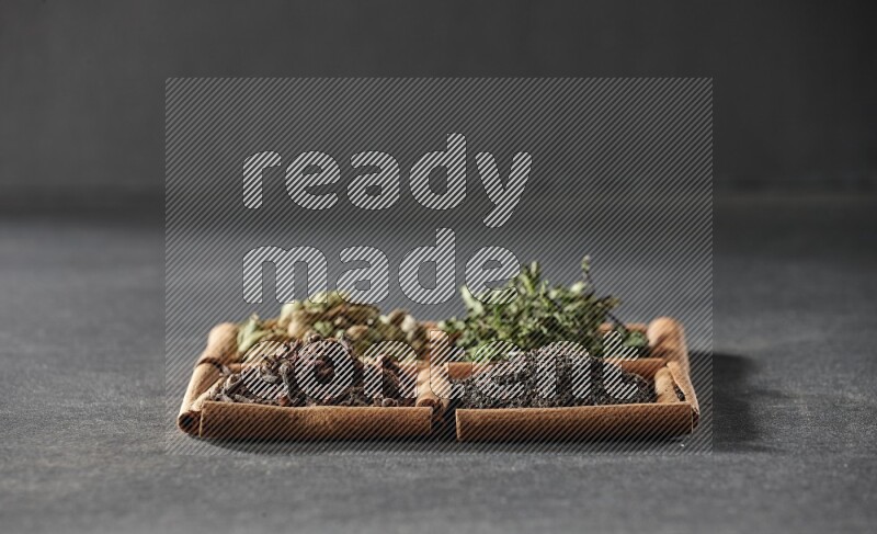 4 مربعات من عيدان القرفة ممتلئة بالشاي الأسود والقرنفل والنعناع المجفف وحبوب الهيل على أرضية سوداء