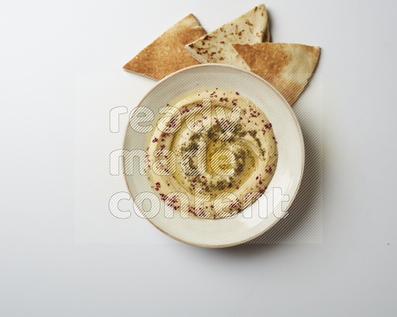 Hummus in a pottry plate garnished with zaatr & sumak on a white background