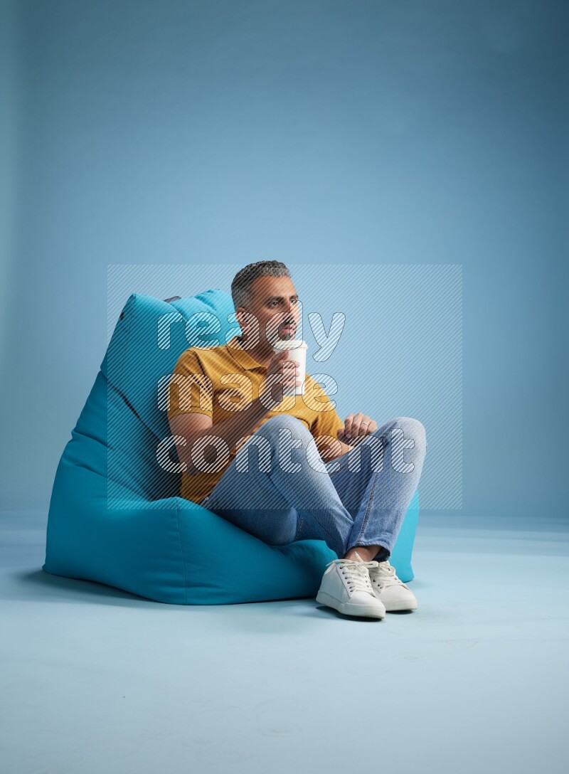A man sitting on a blue beanbag and drinking coffee