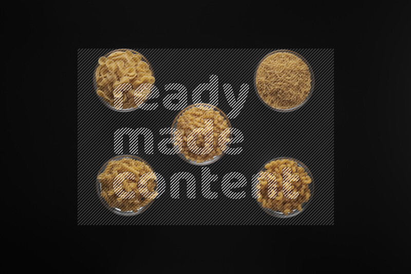 Different pasta types in 5 glass bowls on black background