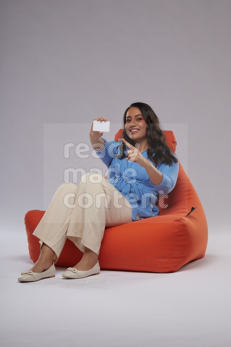 A woman sitting on an orange beanbag and holding ATM card