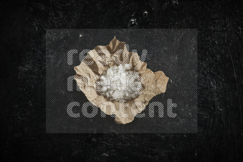 A crumpled piece of paper full of white salt on black background
