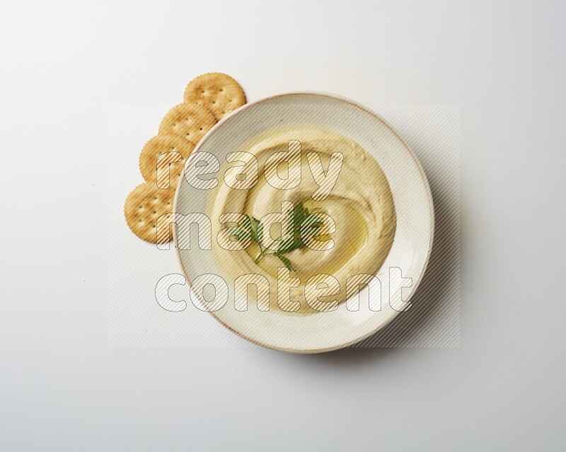Hummus in a pottry plate garnished with parsley on a white back ground