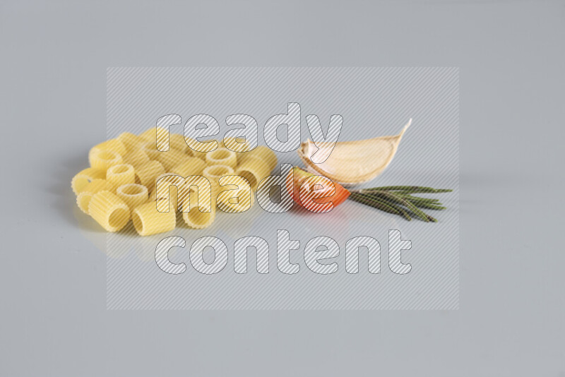 Raw pasta with different ingredients such as cherry tomatoes, garlic, onions, red chilis, black pepper, white pepper, bay laurel leaves, rosemary, cardamom and mushrooms on light blue background