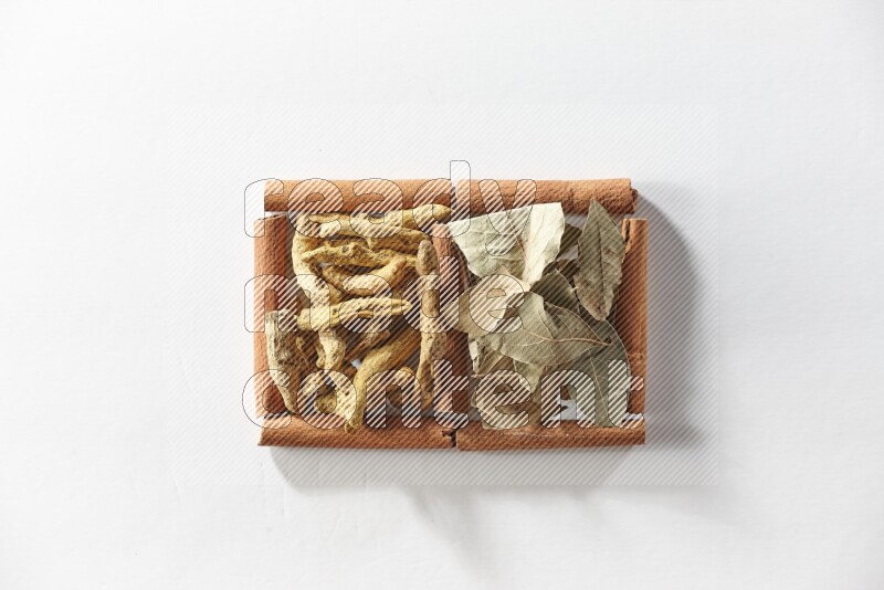 2 squares of cinnamon sticks full of turmeric fingers and bay laurel leaves on white flooring