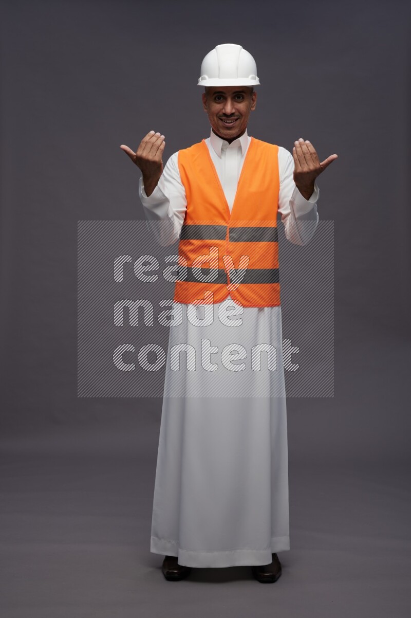 Saudi man wearing thob with engineer vest standing interacting with the camera on gray background