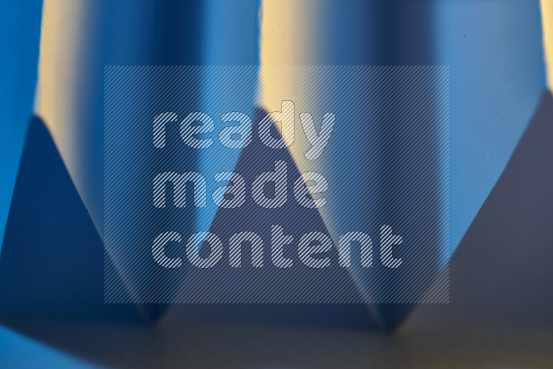 A close-up abstract image showing sharp geometric paper folds in blue gradients and warm tones