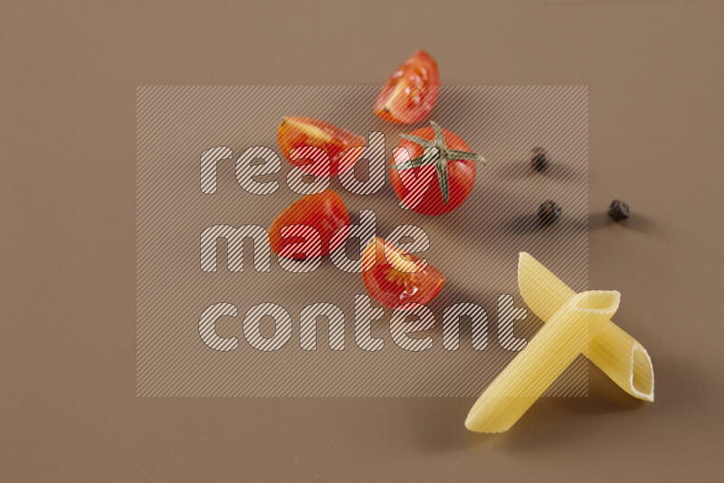 Raw pasta with different ingredients such as cherry tomatoes, garlic, onions, red chilis, black pepper, white pepper, bay laurel leaves, rosemary and cardamom on beige background