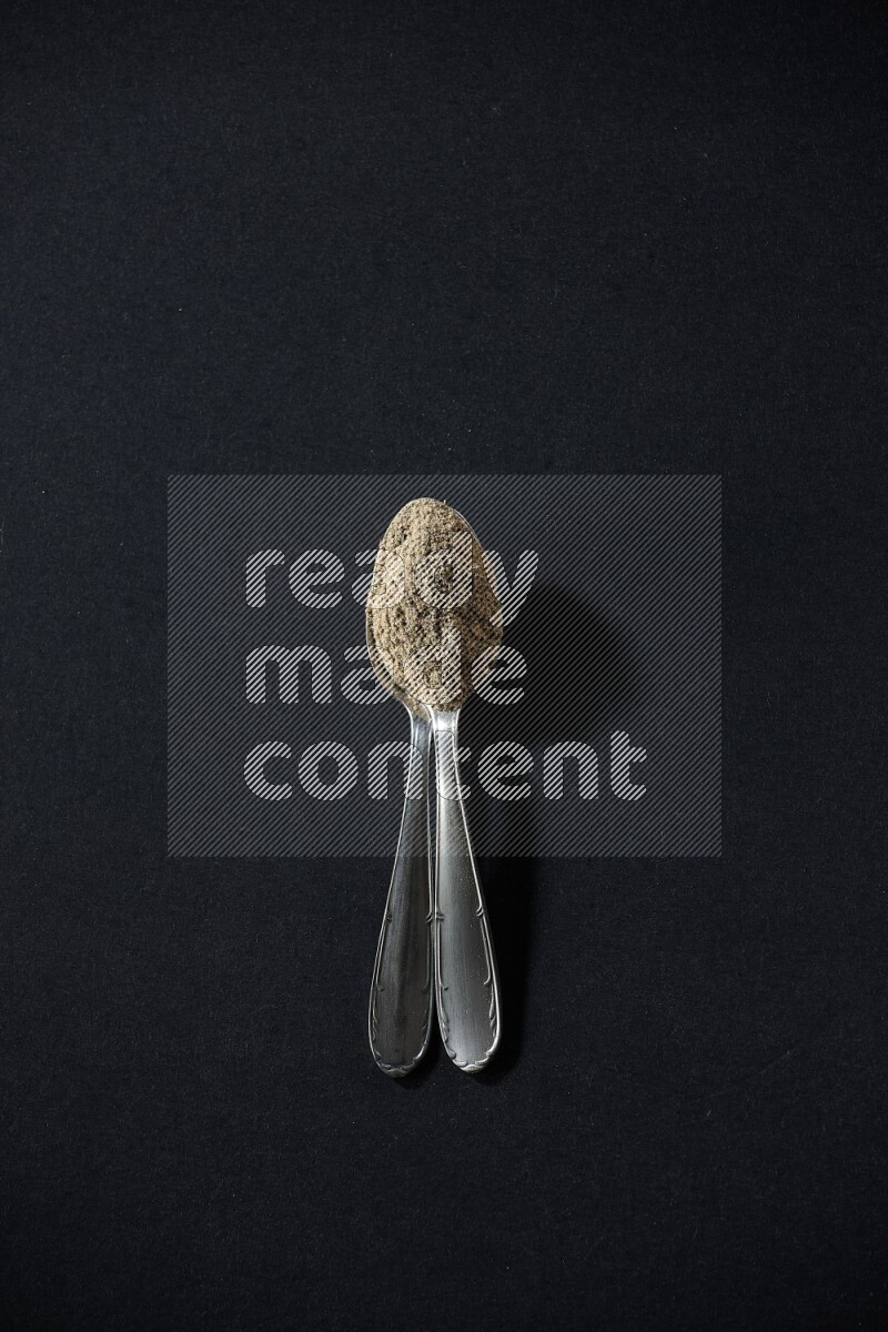 ملعقتان معدنيتان ممتلئتان ببودرة الهيل على خلفية سوداء