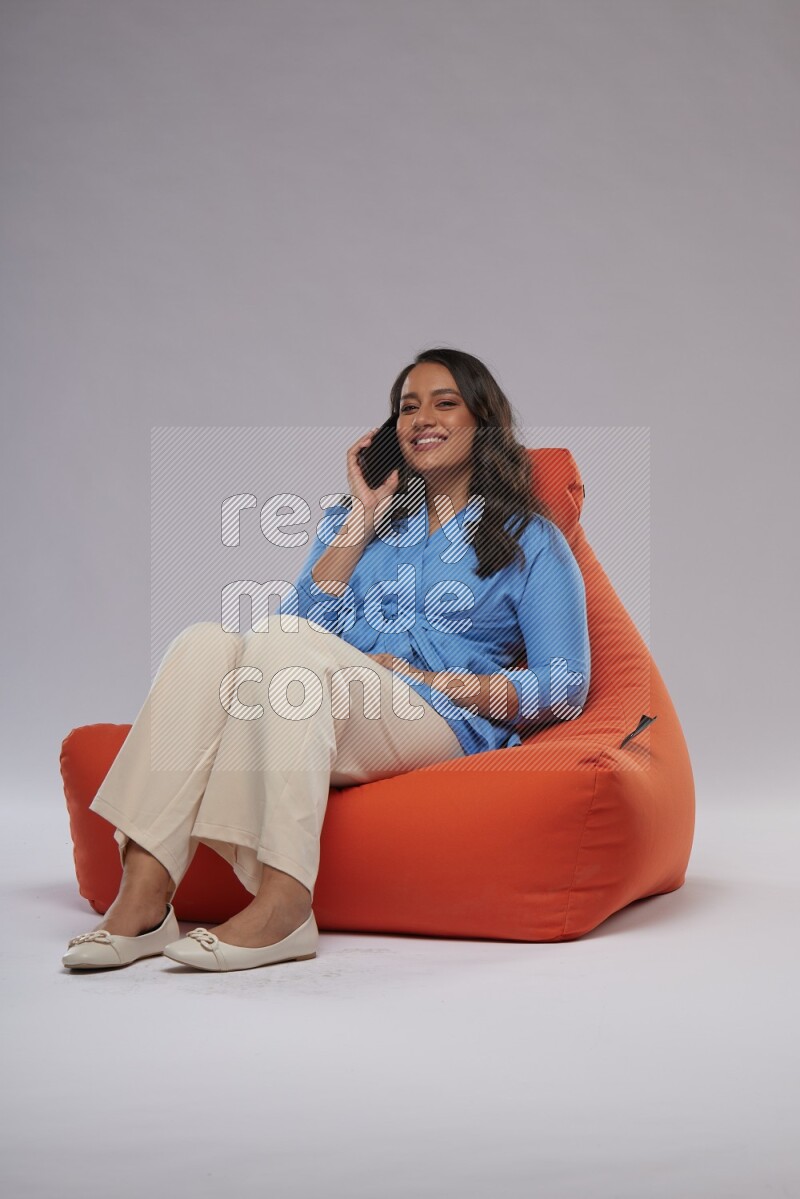 A woman sitting on an orange beanbag and talking on the phone