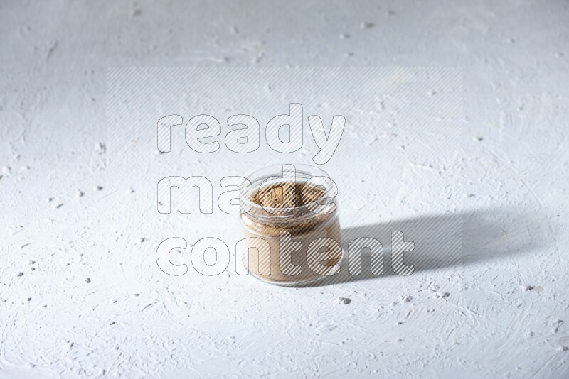 A glass jar full of allspice powder on a textured white flooring