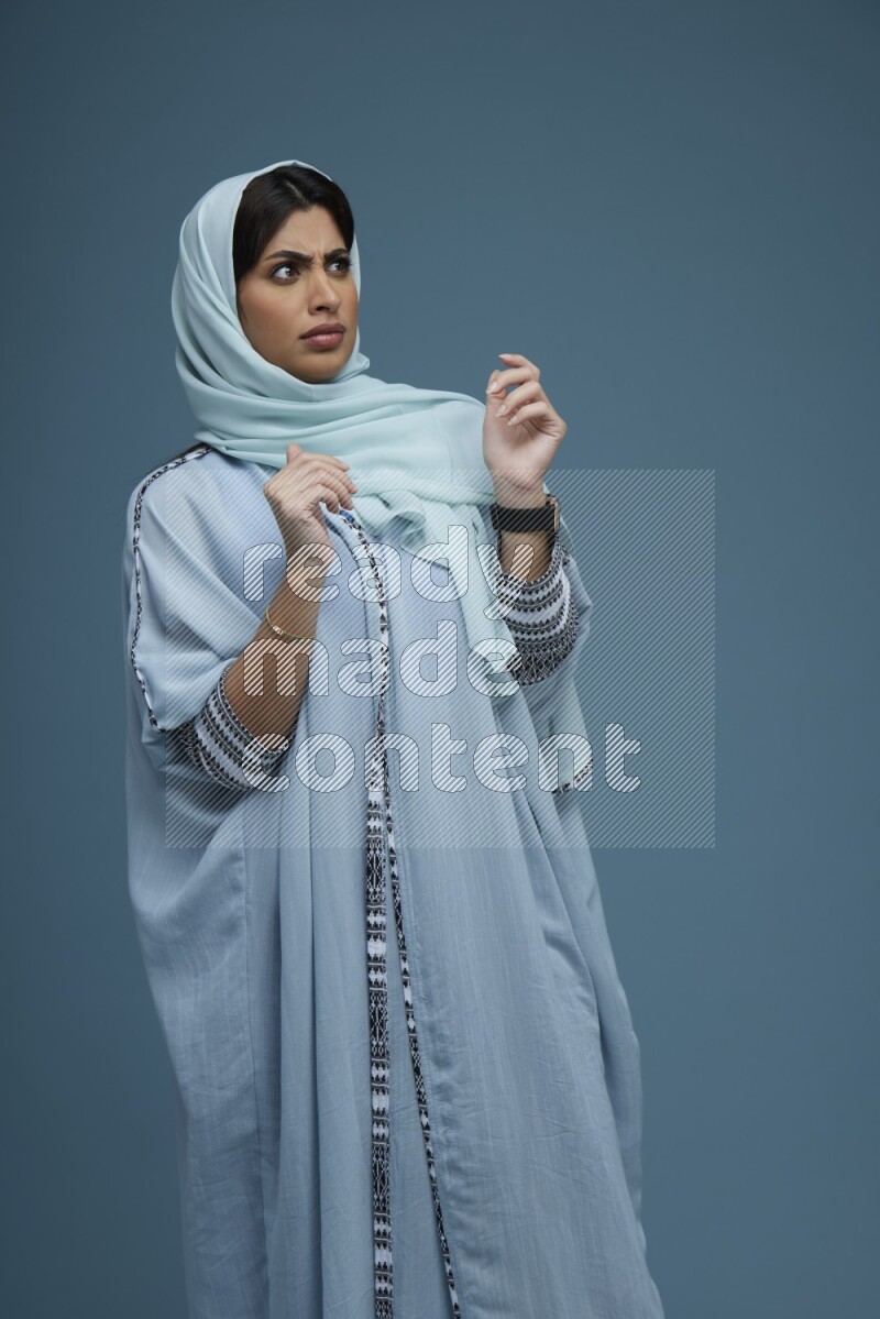A woman posing in a blue background wearing a blue Abaya with hijab