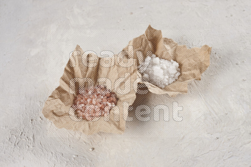 2 crumpled pieces of paper full of pink himalayan salt and white salt on white background