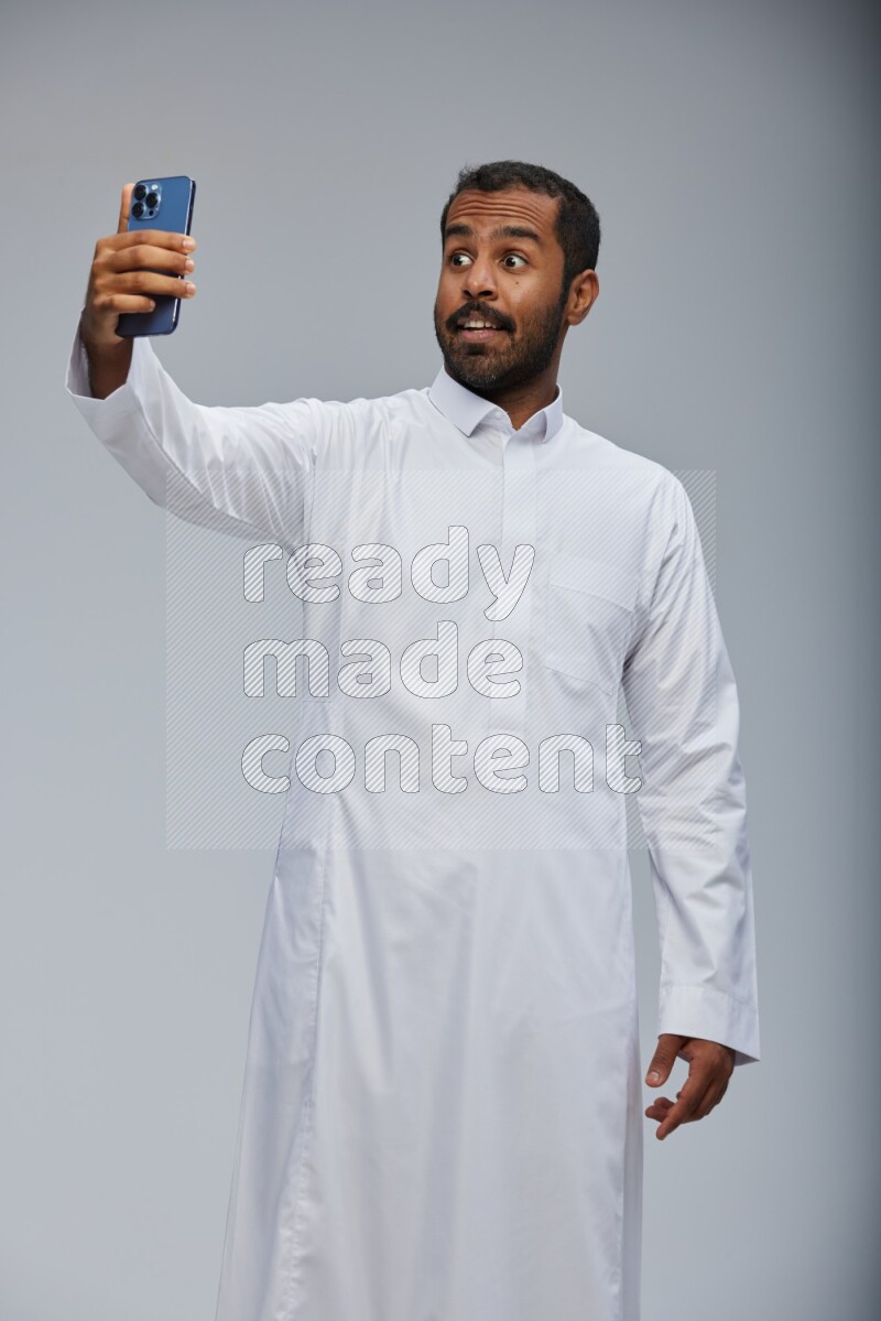 Saudi man wearing Thob standing taking selfie on Gray background