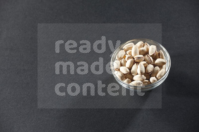 A glass bowl full of pistachios on a black background in different angles