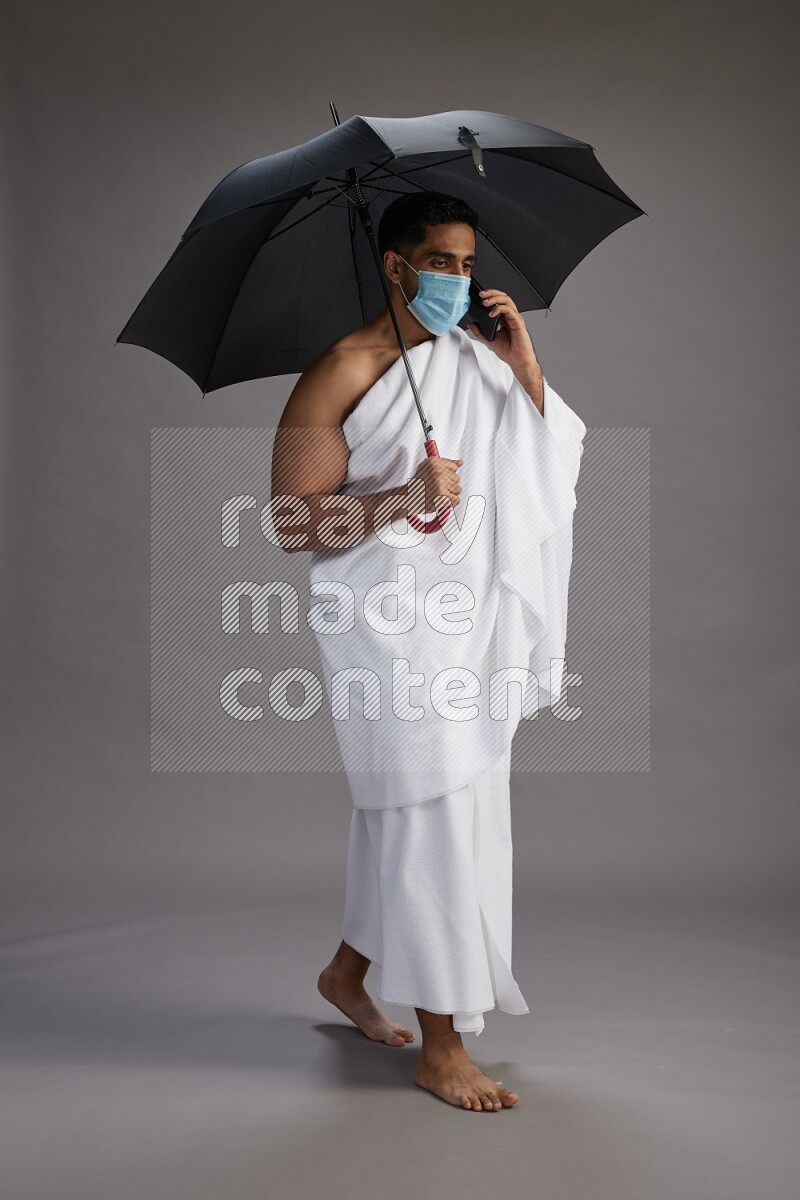 A man wearing Ehram and mask Standing holding umbrella on gray background on gray background