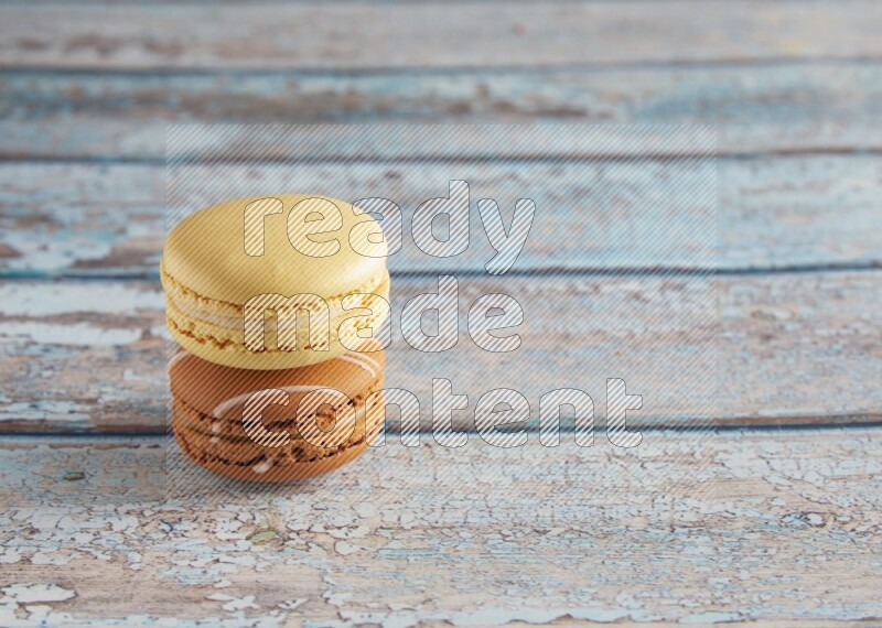 45º Shot of of two assorted Brown Irish Cream, and Yellow Vanilla macarons on light blue background