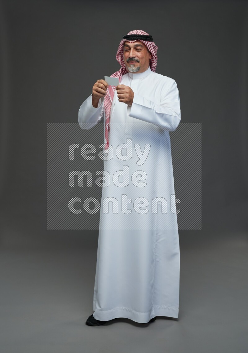 Saudi man with shomag Standing holding ATM card on gray background