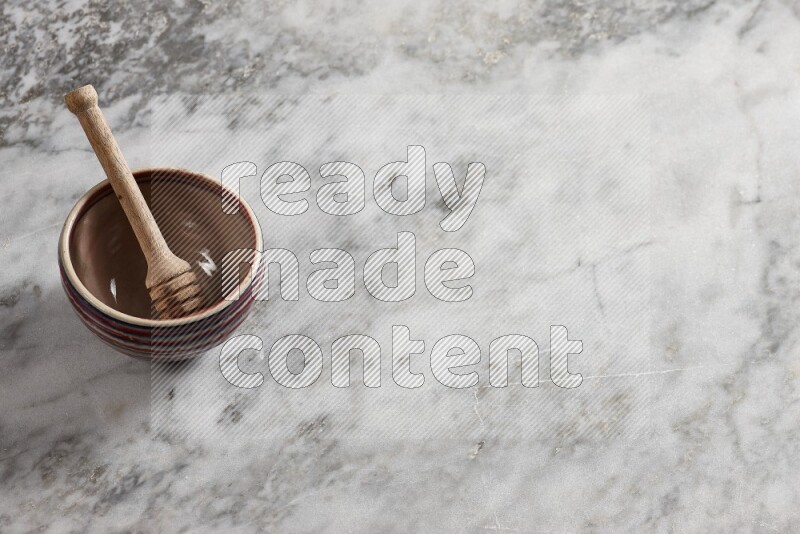 Multicolored pottery bowl with wooden honey dipper in it on grey marble background