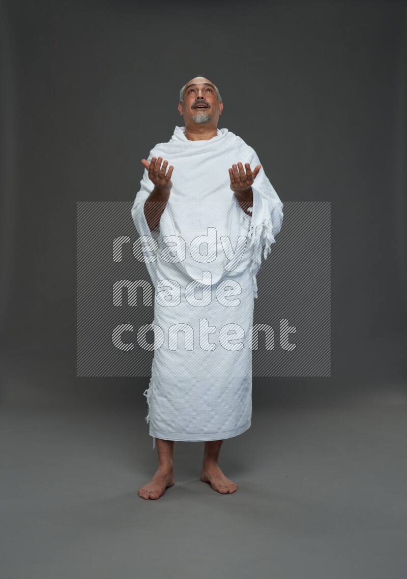 A man wearing Ehram Standing dua'a on gray background