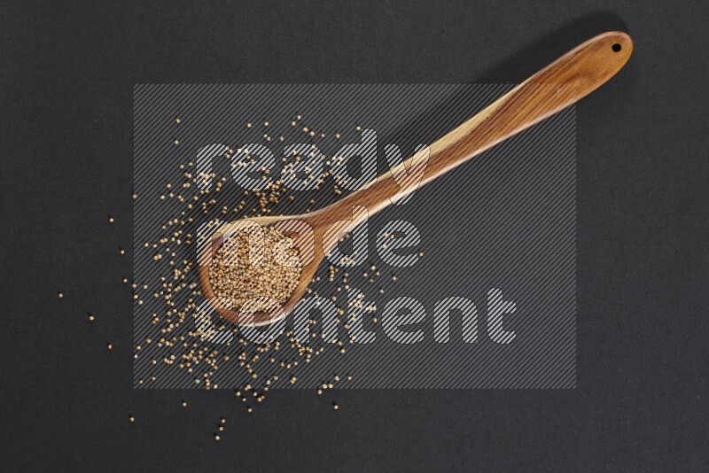 A wooden spoon full of mustard seeds on a black flooring