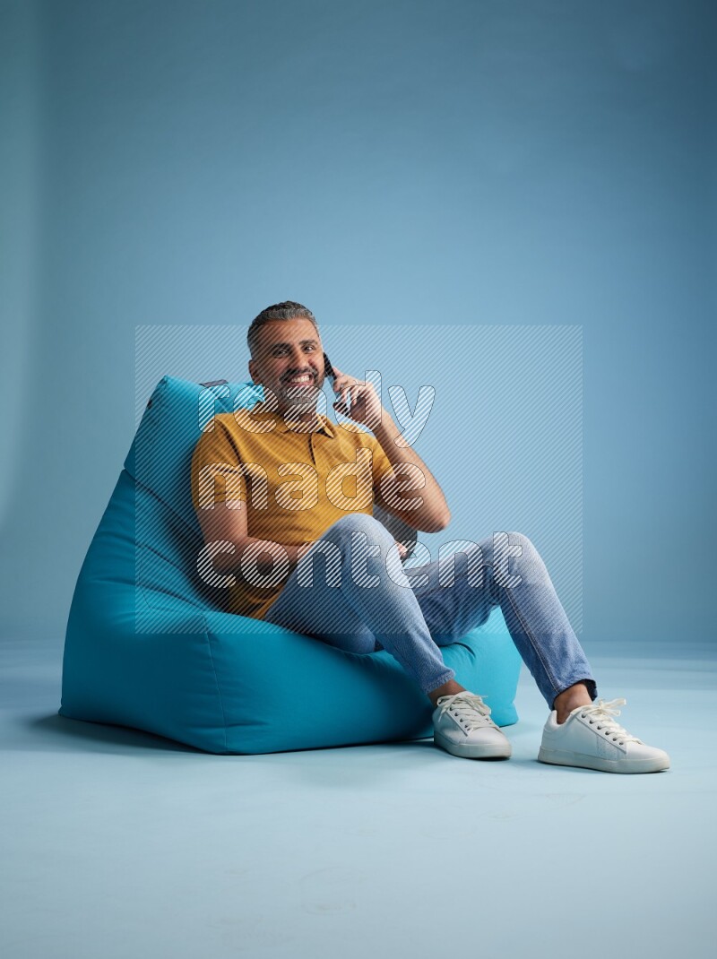 A man sitting on a blue beanbag and talking on the phone