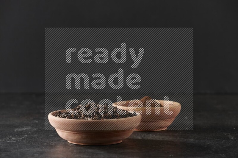 2 wooden bowls full of cloves powder and whole cloves on a textured black flooring
