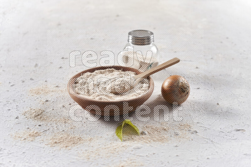 A wooden bowl full of onion powder with a glass jar beside it and fresh onion on white background