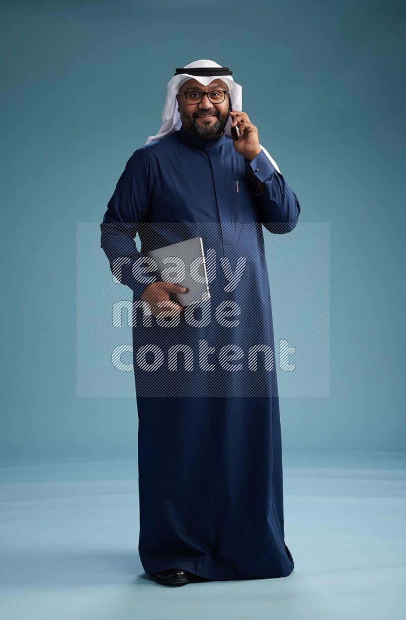 Saudi Man with shimag Standing talking on phone on blue background
