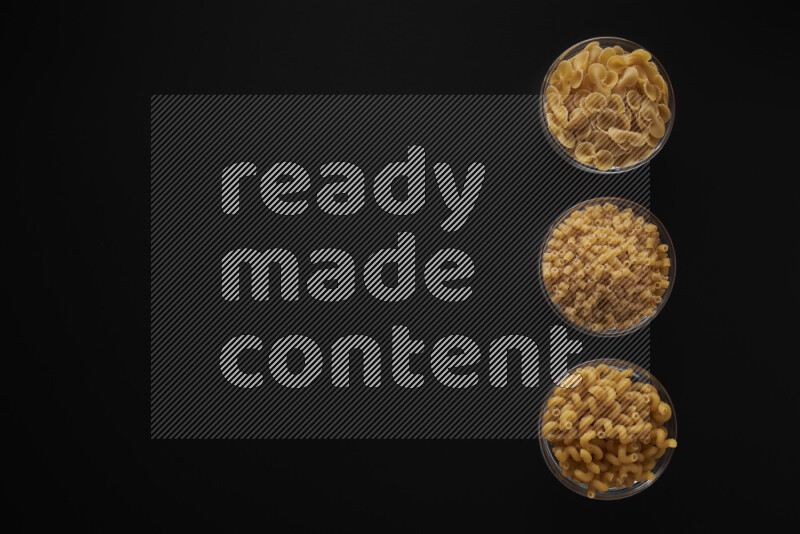 Different pasta types in 3 glass bowls on black background