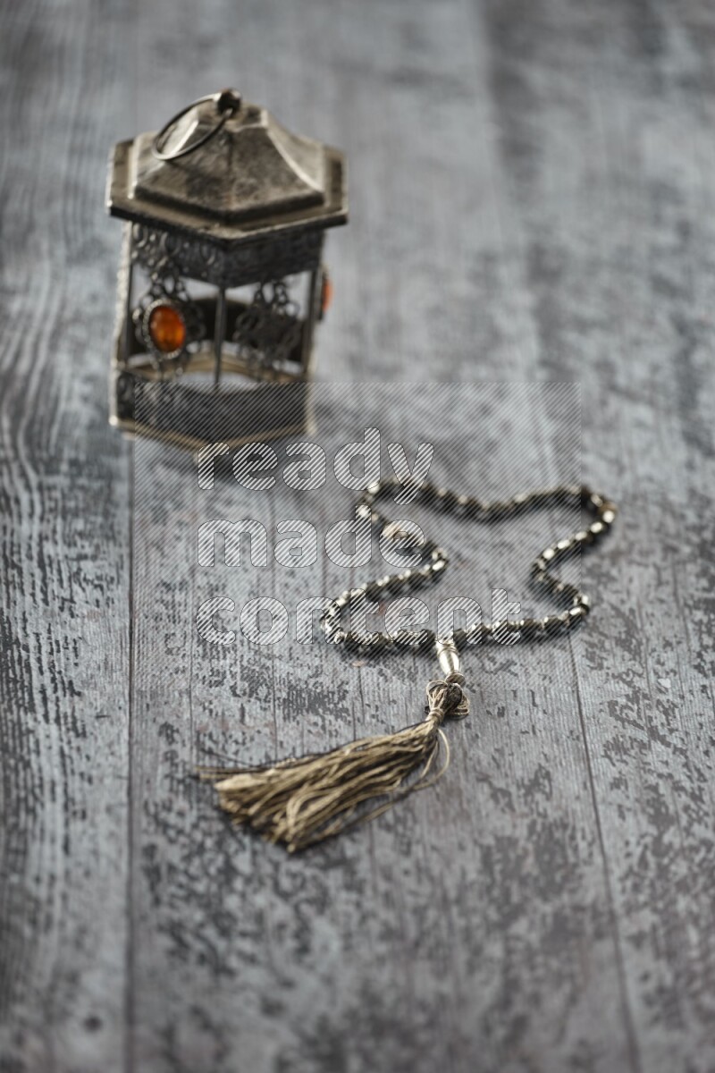 A silver lantern with different drinks, dates, nuts, prayer beads and quran on grey wooden background