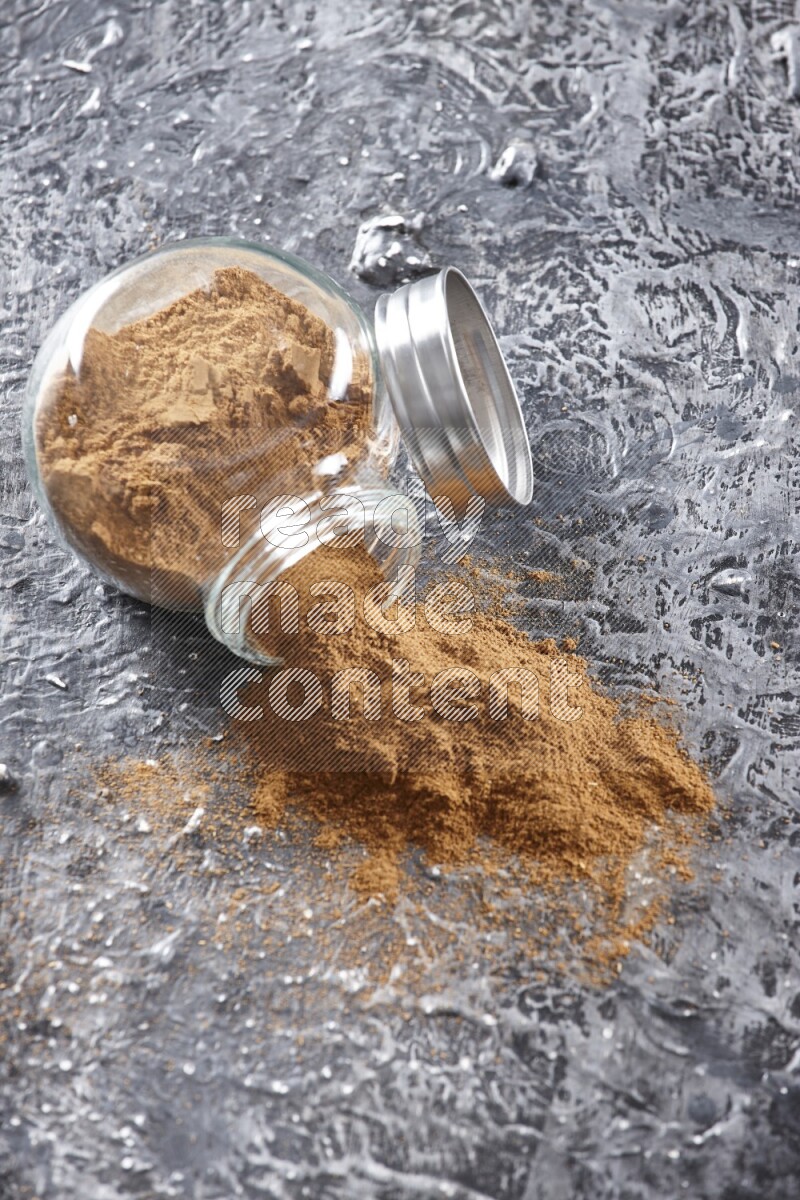 Flipped herbal glass jar full of cinnamon powder on textured black background