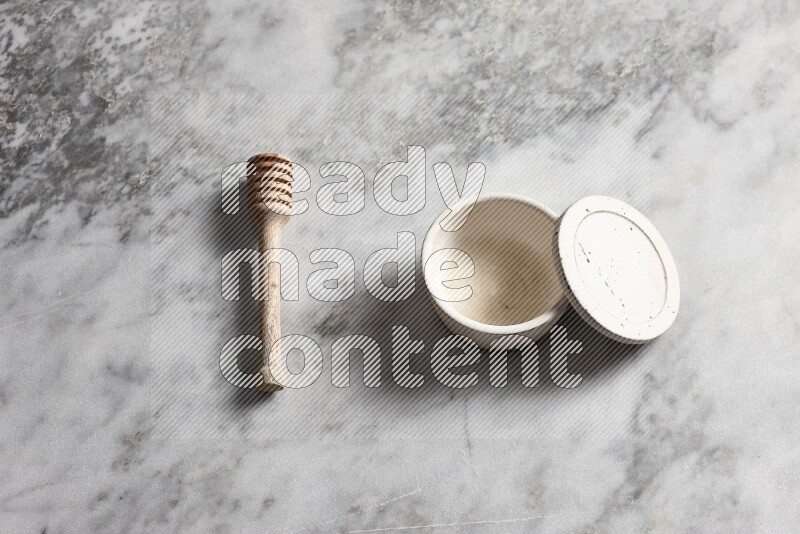 White pottery bowl with wooden honey dipper on the side on grey marble background