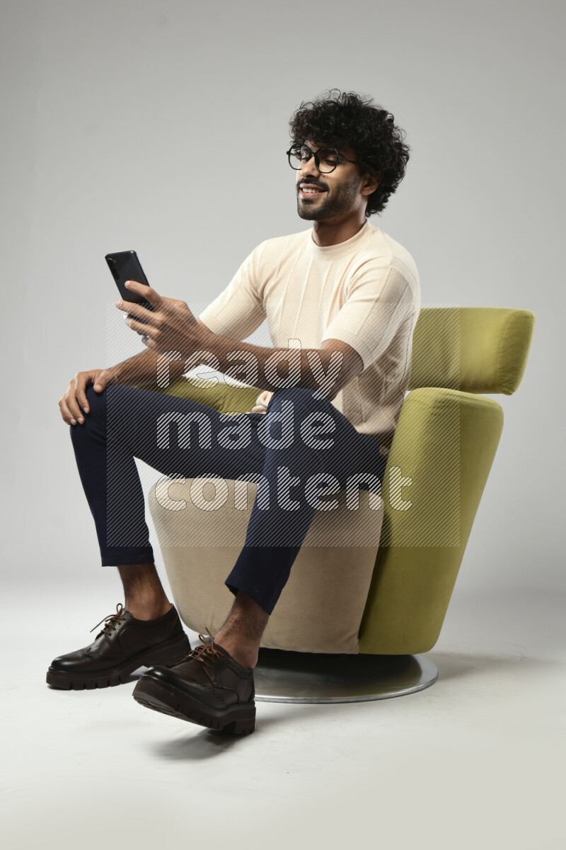 A man wearing casual sitting on a chair browsing on the phone on white background