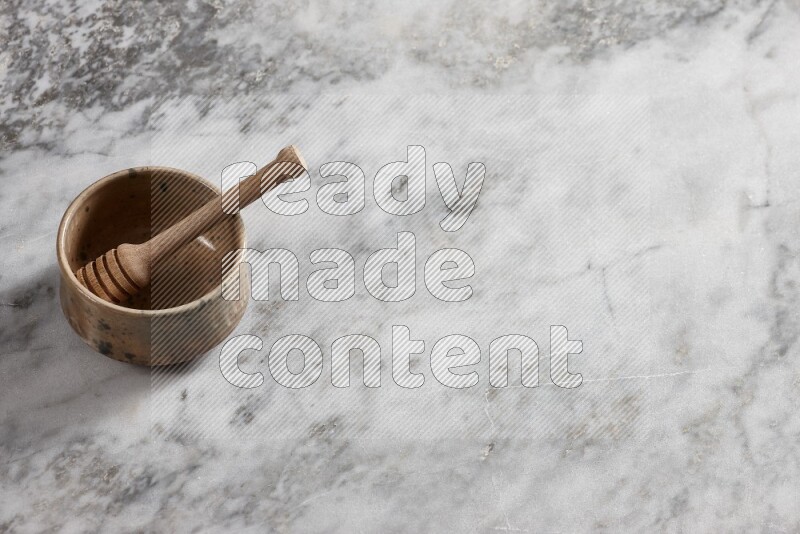 Multicolored pottery bowl with wooden honey dipper in it on grey marble background