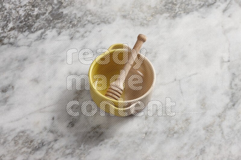 Multicolored pottery bowl with wooden honey dipper in it on grey marble background