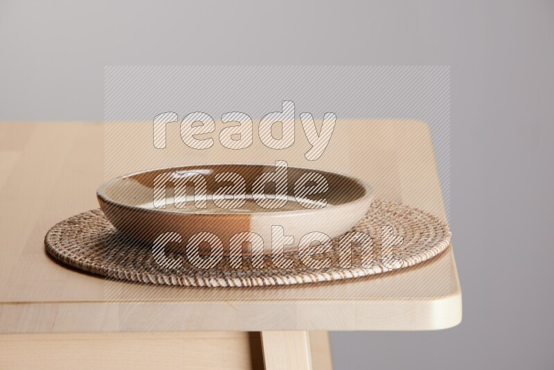multi-colored pottery Plate placed on a big light colored straw placemat on the edge of wooden table